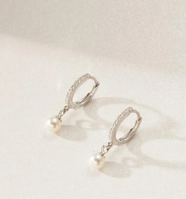 Sterling Silver Diamante Pearl Earrings flat down on a shiny, glittery surface.